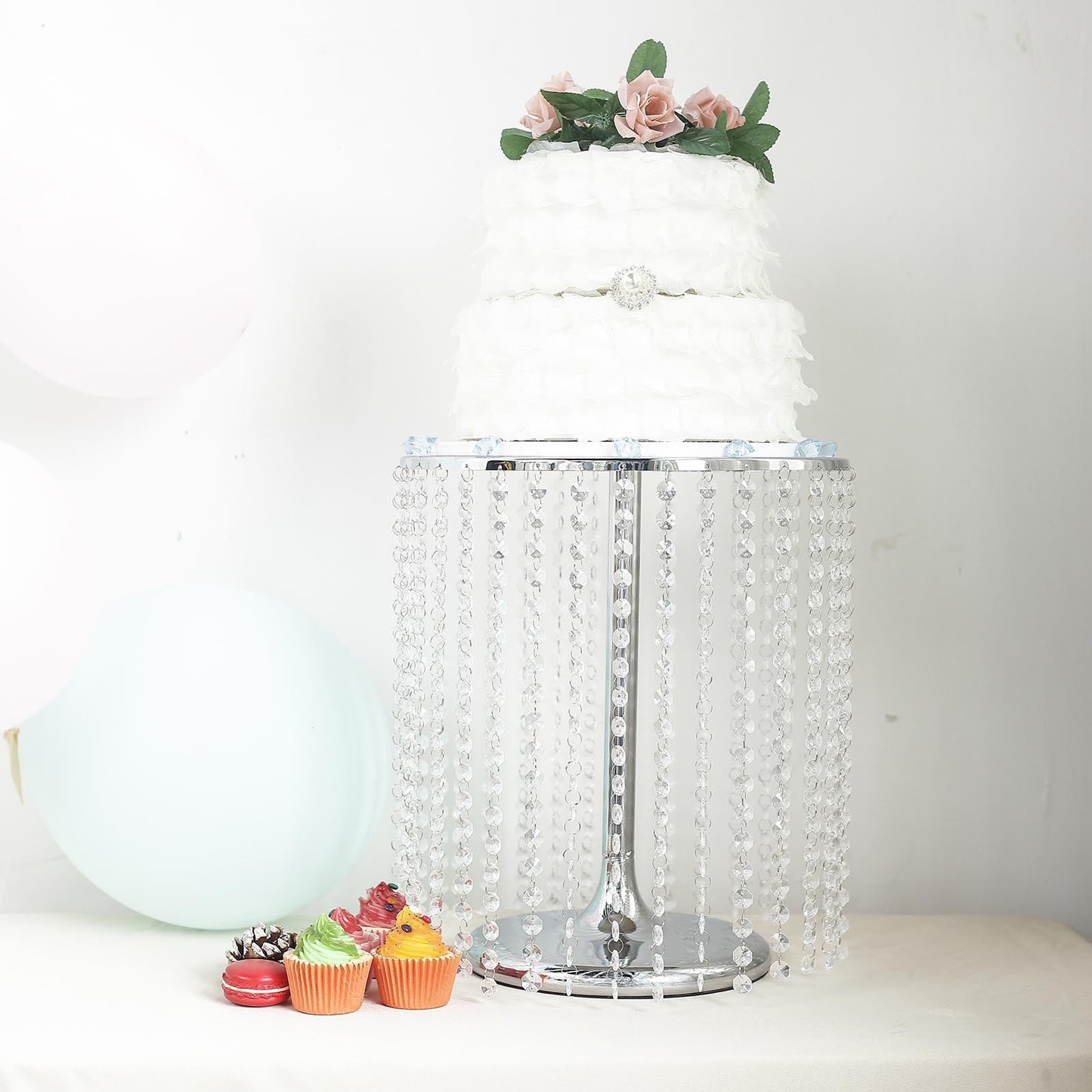 Metallic silver cake stand with crystal chains displaying a decorated cake and cupcakes.