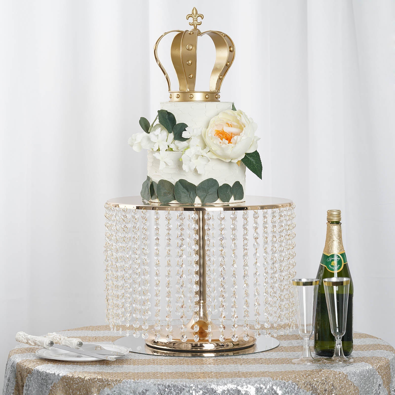 Metallic gold cake stand with crystal chains, featuring a crown cake and floral decor.