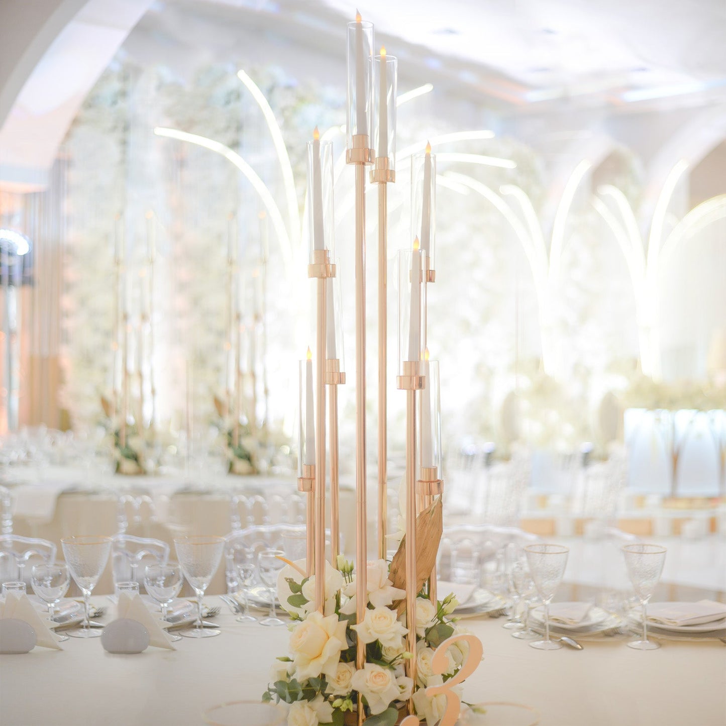 Gold 8 arm taper candle holder with clear glass shades and floral arrangement.
