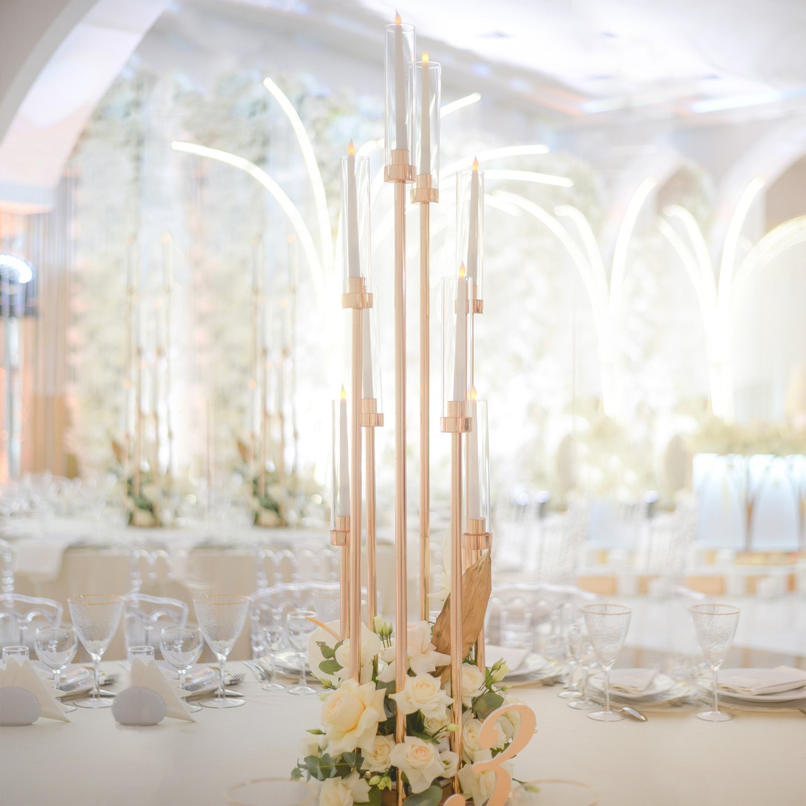 Gold 8 arm taper candle holder with clear glass shades and floral arrangement.