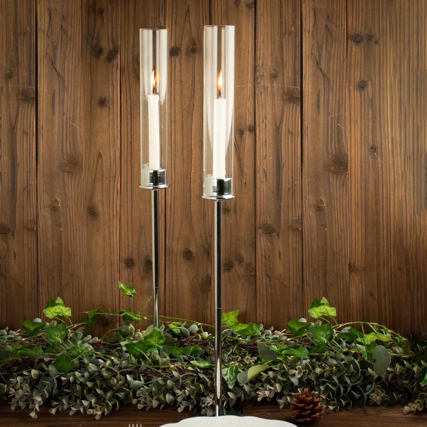 24" tall silver metal candlestick holders with glass chimneys, featuring lit candles.