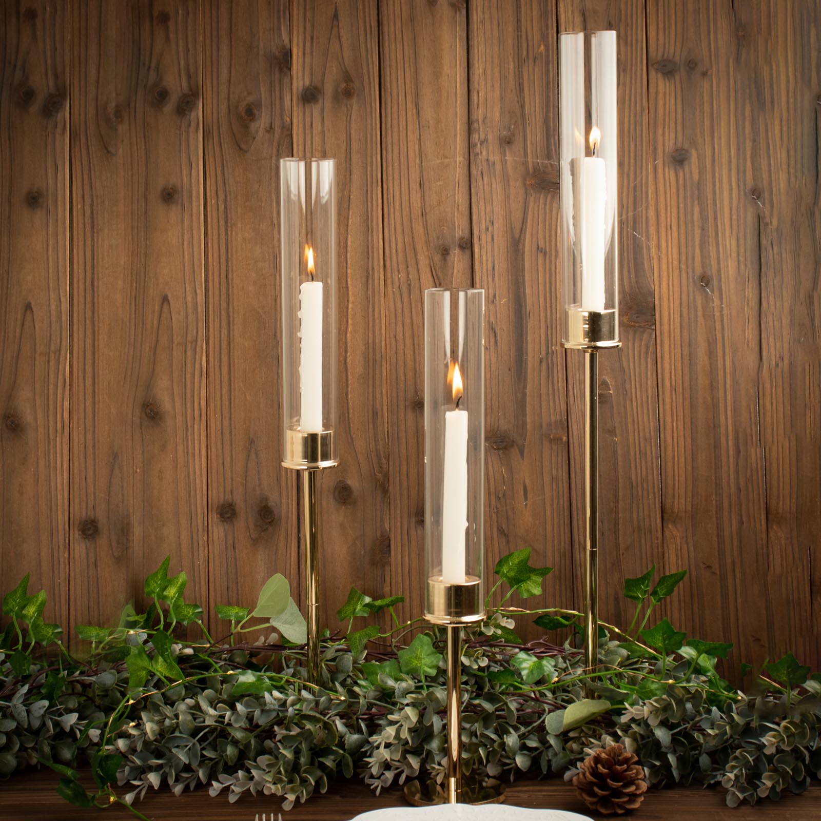 Tall gold candlestick holders with clear glass chimneys and lit candles.