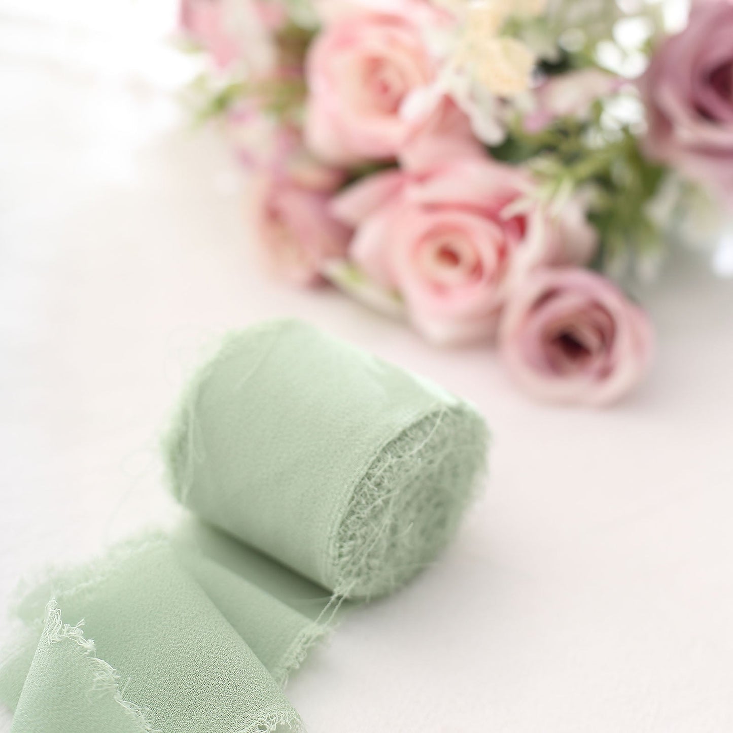 Sage green chiffon ribbon roll next to a bouquet of pink roses.