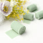 Sage green chiffon ribbon rolls on a white surface with floral accents.