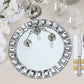 Silver jeweled rim glass mirror charger plate on a table setting.