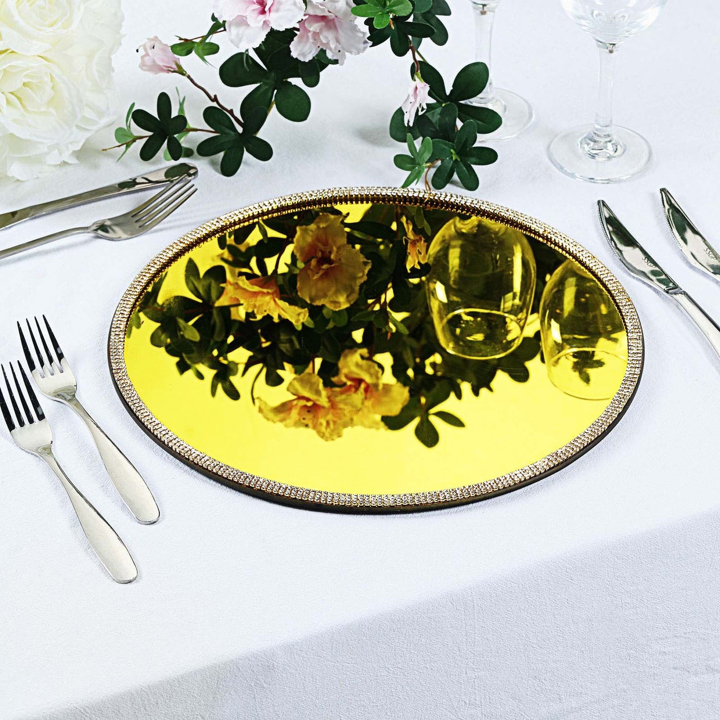 Metallic gold mirror charger plate with rhinestone rim on a table setting.