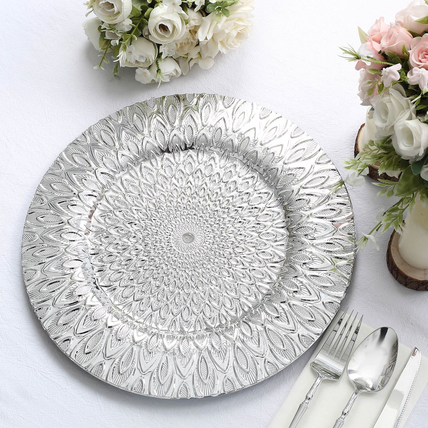 Silver embossed peacock design disposable charger plate on a white tablecloth.