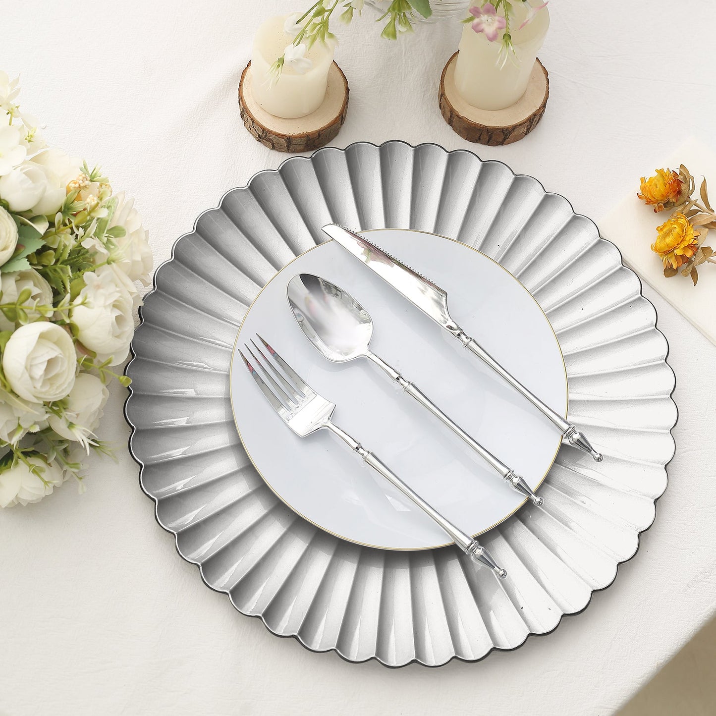 Silver scalloped shell pattern charger plate with utensils on a table setting.