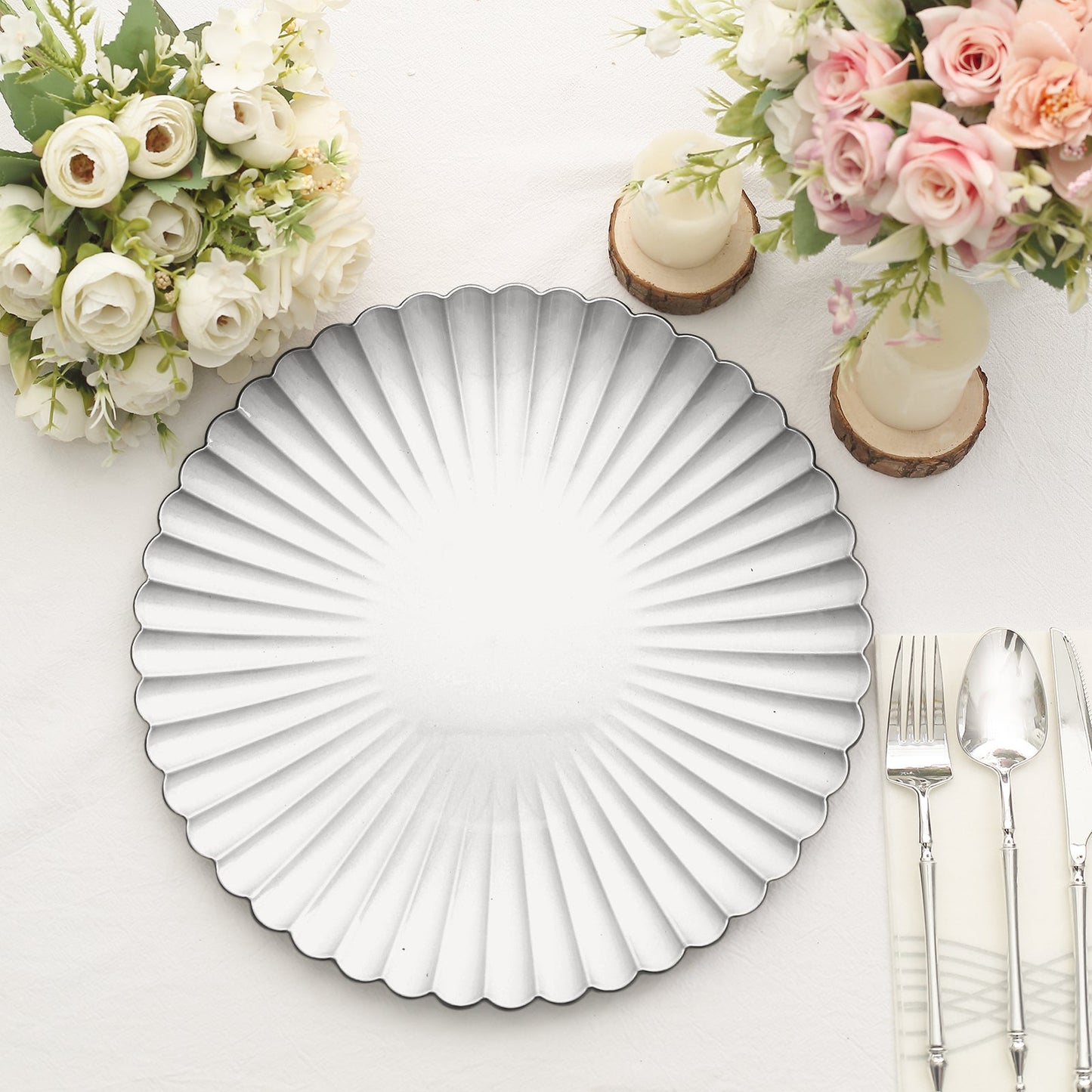 Silver scalloped shell pattern plastic charger plate on a table setting.