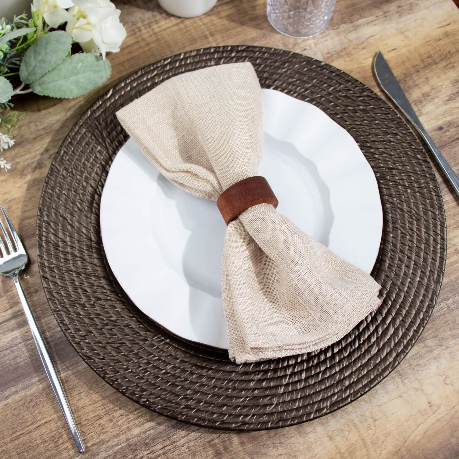 Natural brown rattan-like disposable round charger plate on a table setting.