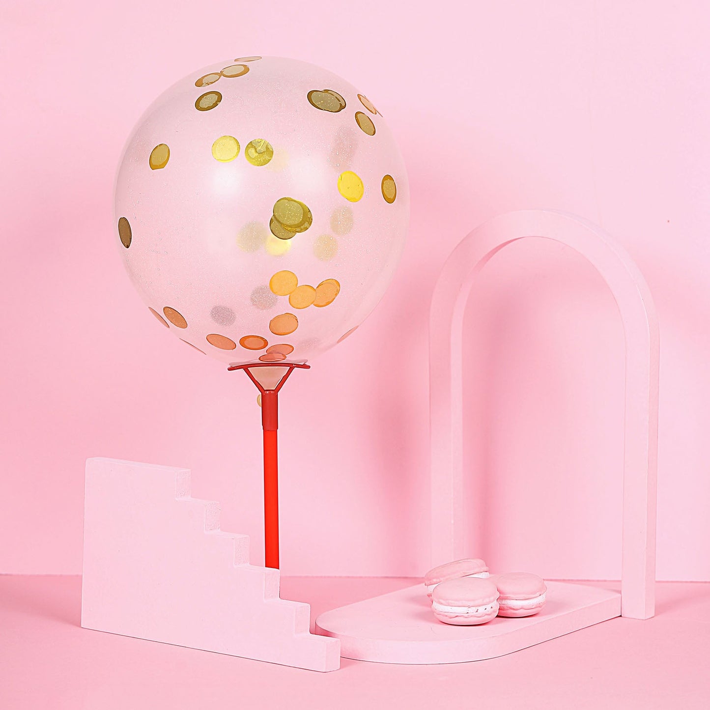 Gold round foil metallic table confetti dots with balloon decor on pink background.