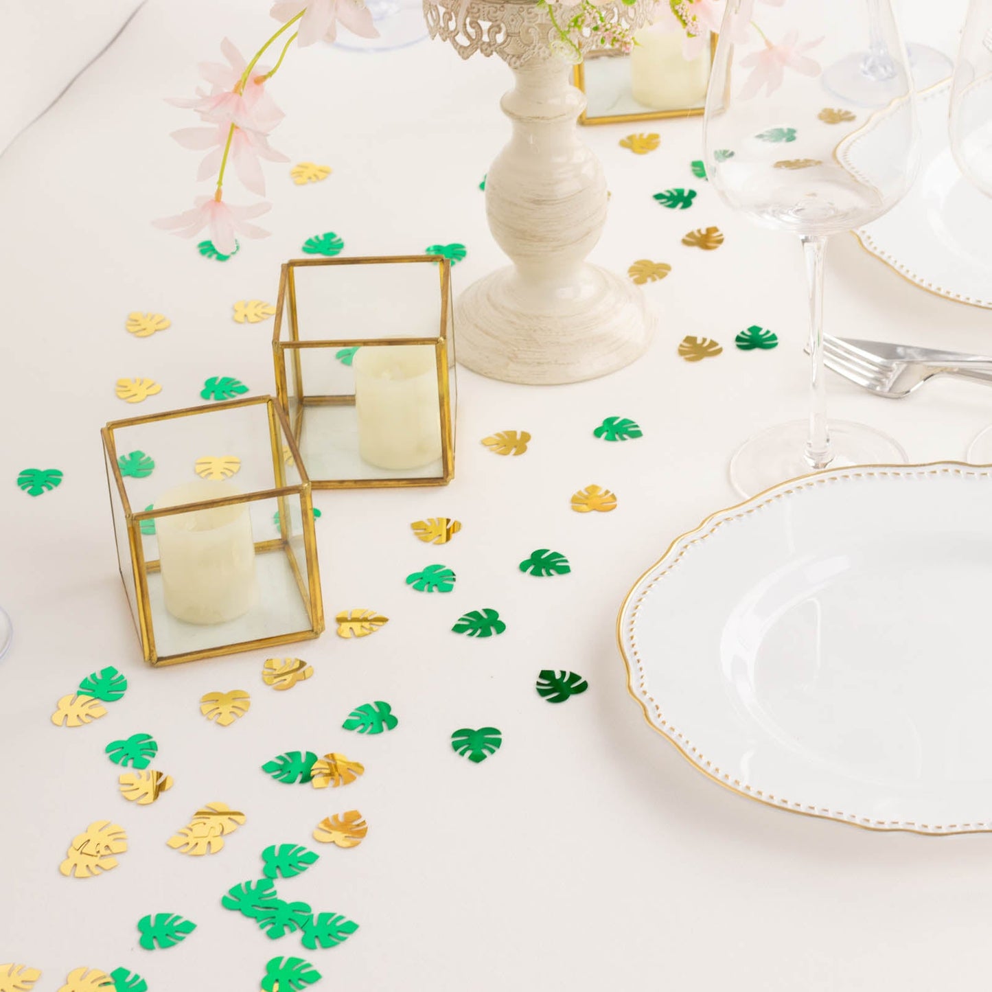 Metallic green and gold tropical palm leaf table confetti scattered on a table.