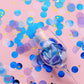 Purple and blue tissue paper and foil confetti on a pink background.