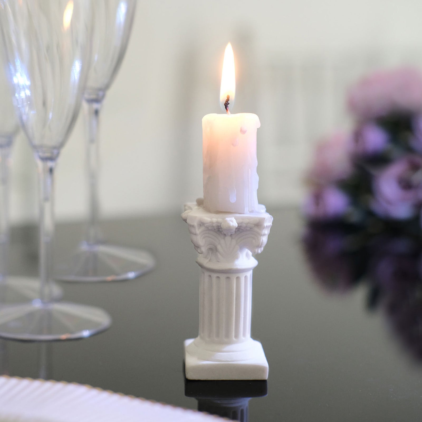 White Roman column candle holder pedestal with lit candle.