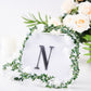 Black decorative rhinestone letter "N" surrounded by greenery and flowers.