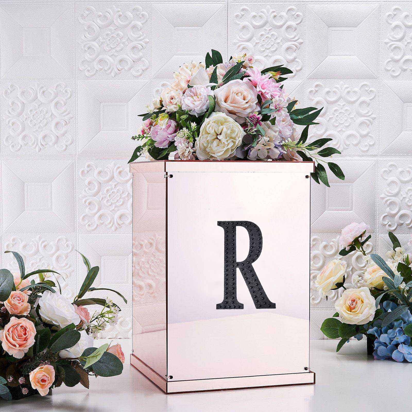 Black rhinestone letter "R" sticker on a decorative box with flowers.