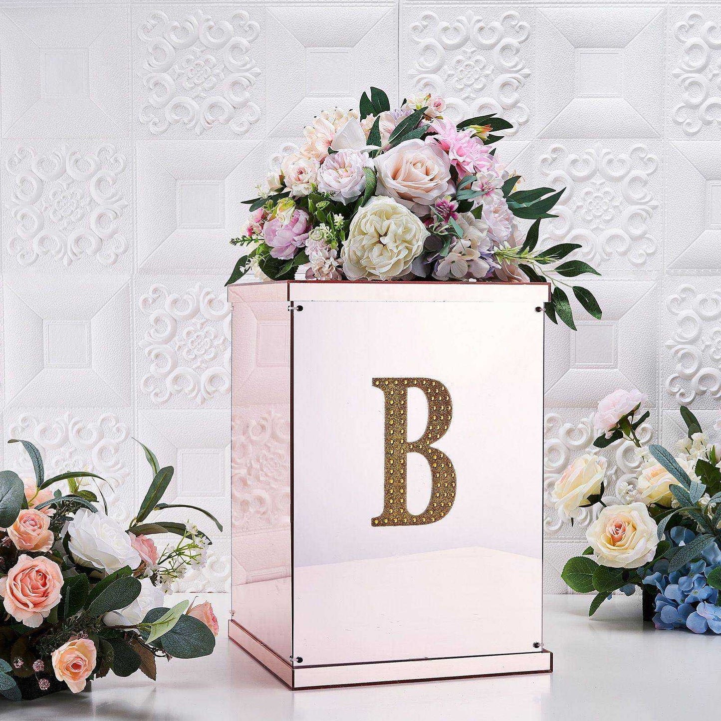 Gold decorative rhinestone letter "B" on a mirrored box with floral arrangements.
