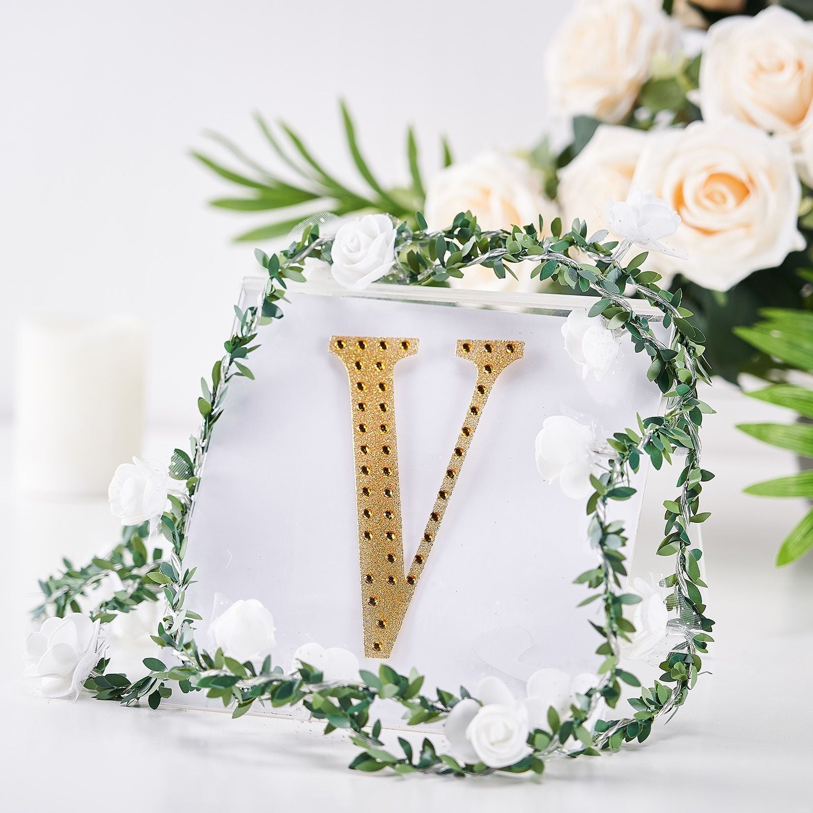 Gold decorative rhinestone letter "V" surrounded by floral accents.