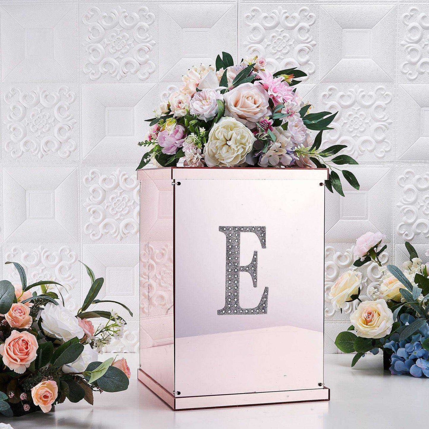 Silver decorative rhinestone letter "E" on a mirrored box with floral arrangements.