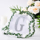 Silver decorative rhinestone letter "G" with floral accents.