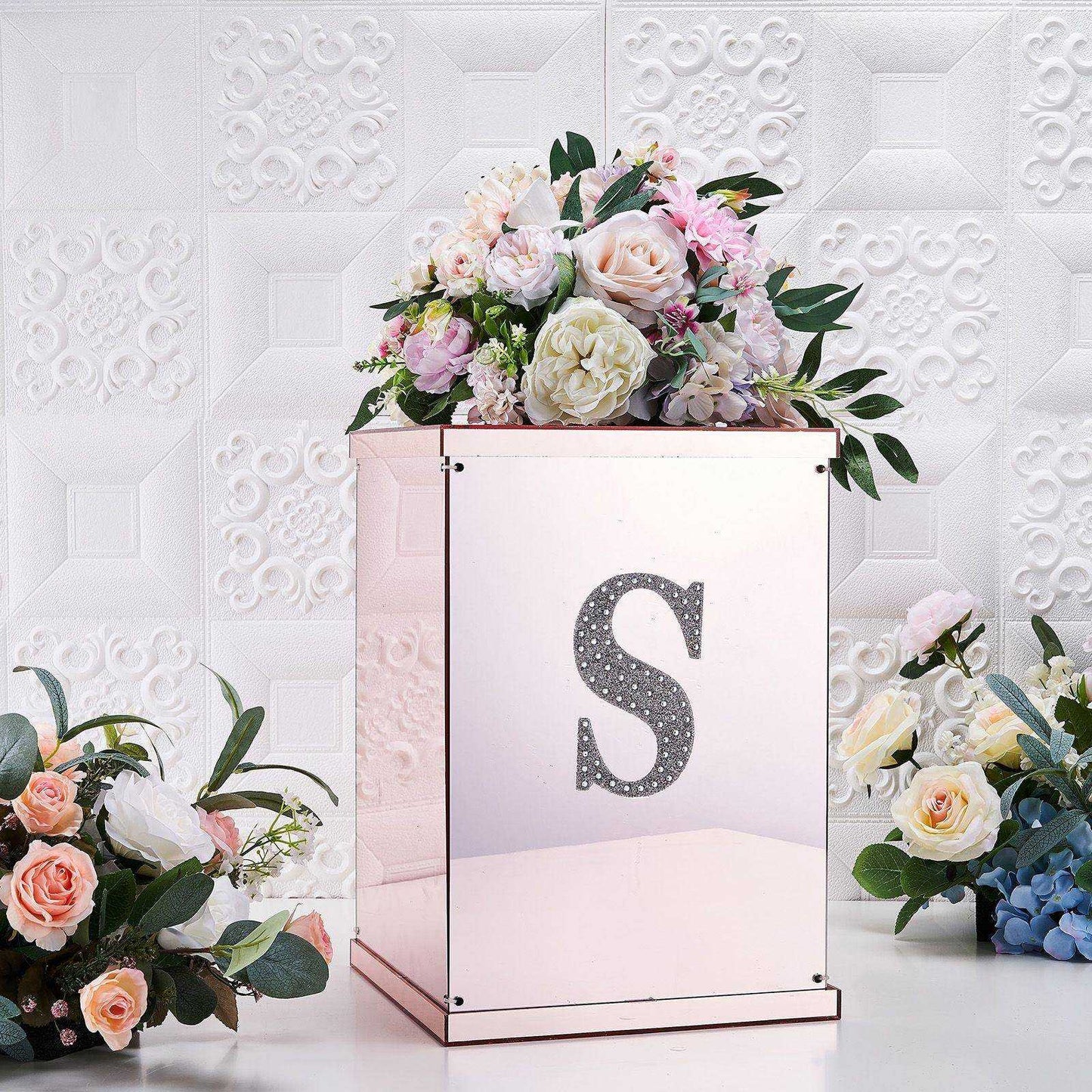 Silver decorative rhinestone letter "S" on a mirrored box with flowers.