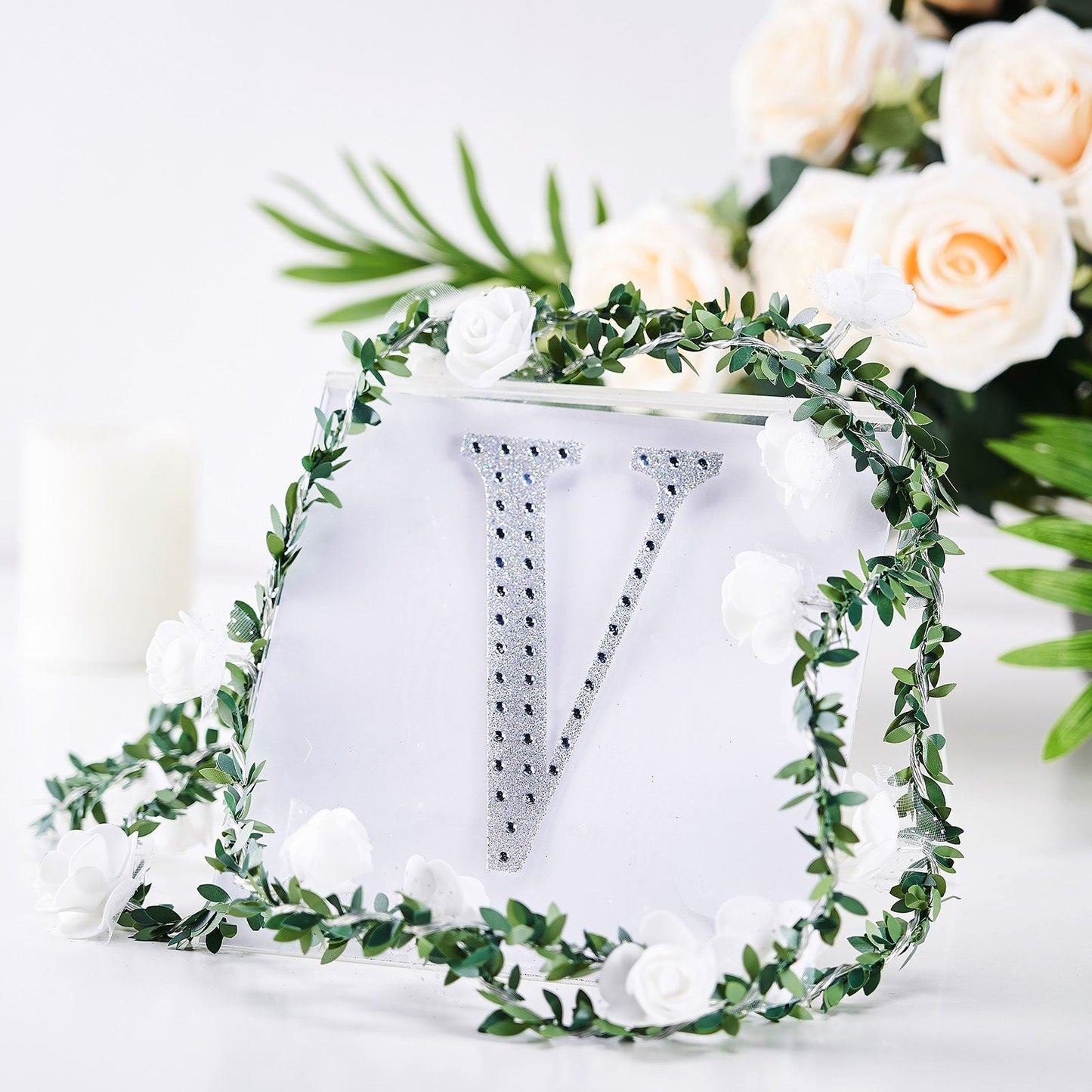 Silver decorative rhinestone letter "V" surrounded by floral accents.