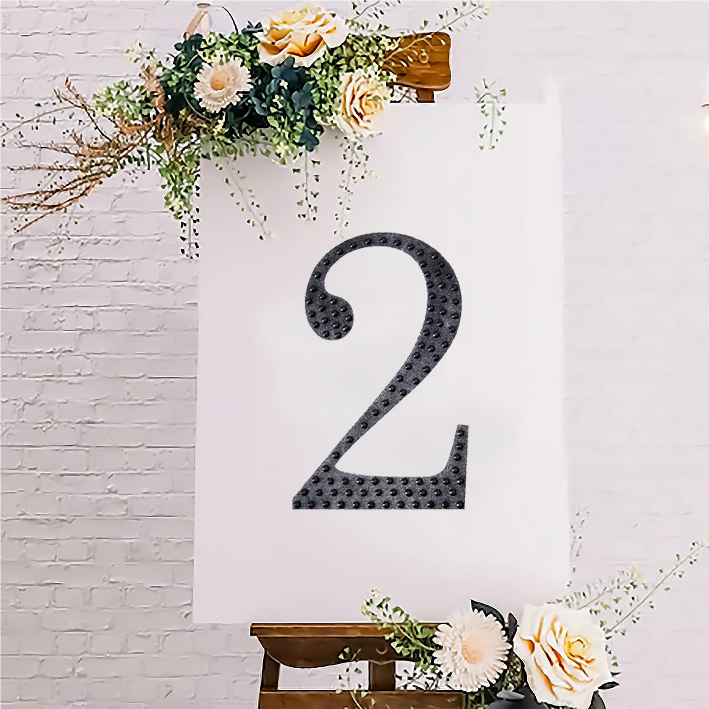 Black decorative rhinestone number "2" sticker on a display with flowers.