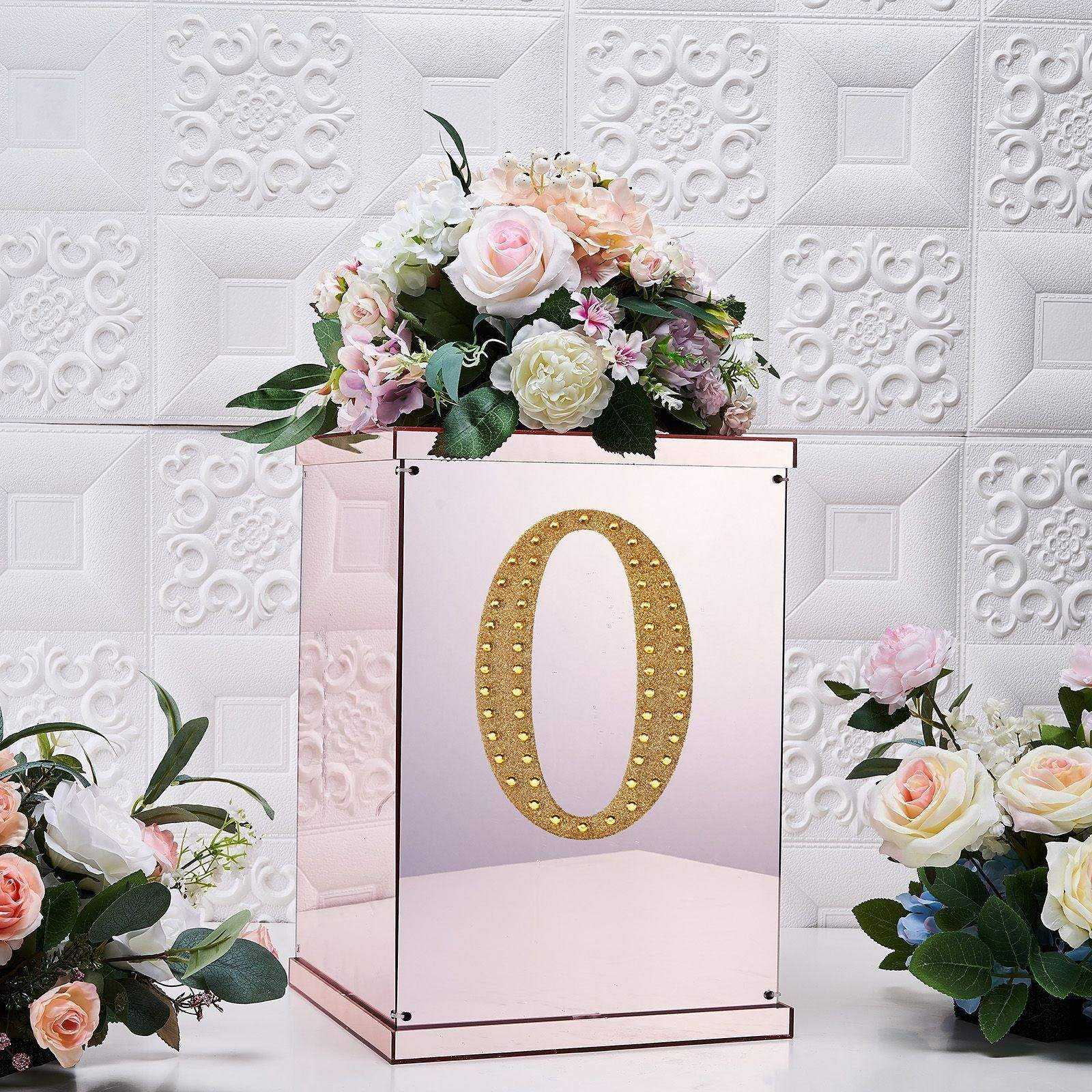Gold decorative rhinestone letter "O" on a mirrored box with flowers.