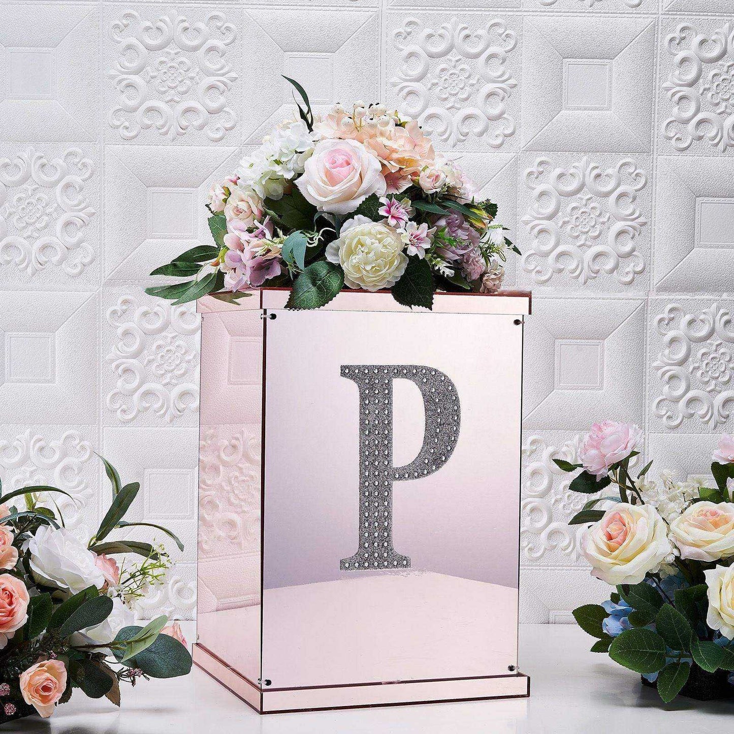 Silver decorative rhinestone letter "P" on a floral arrangement backdrop.