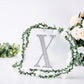 Silver decorative rhinestone letter "X" surrounded by flowers and greenery.