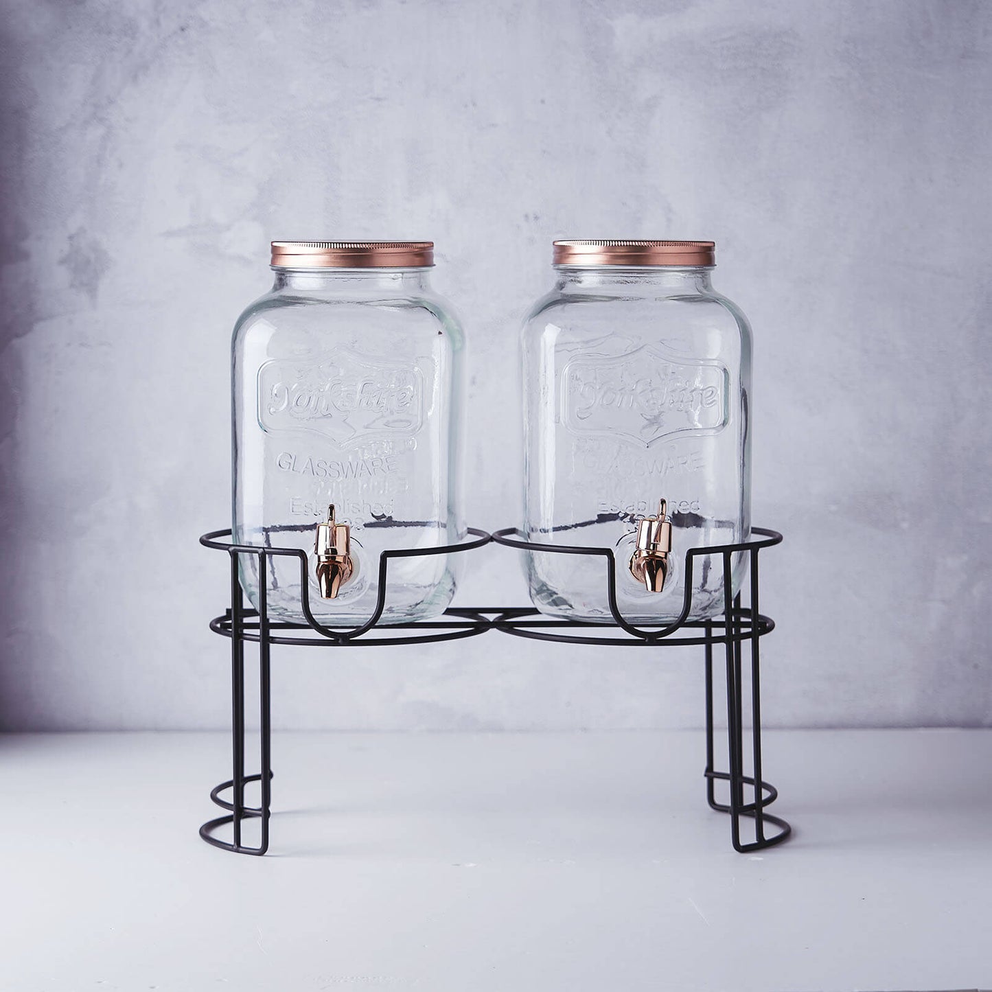 Clear dual gallon glass jars dispenser with rose gold lids.