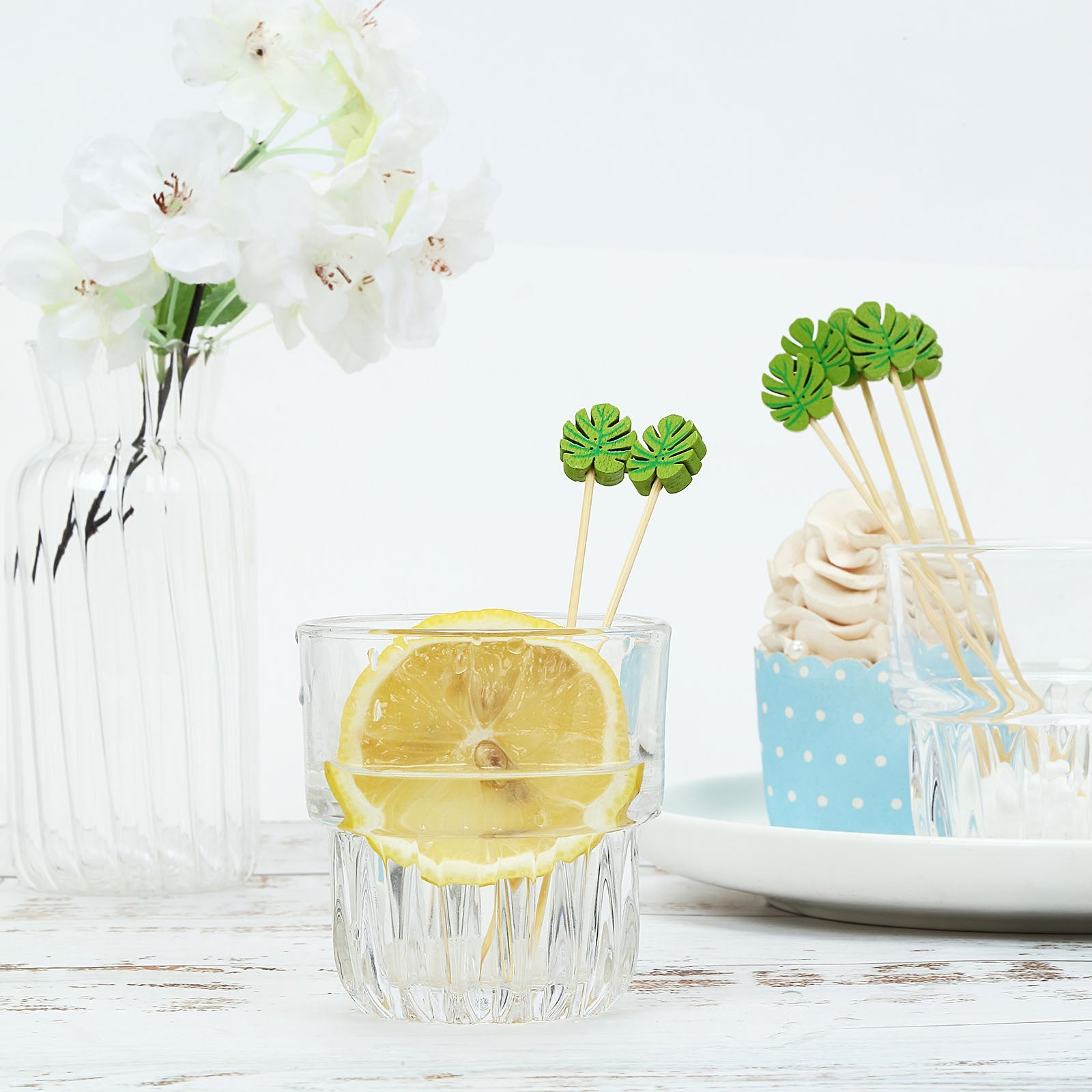 Green tropical leaf party picks in a glass with lemon slice.