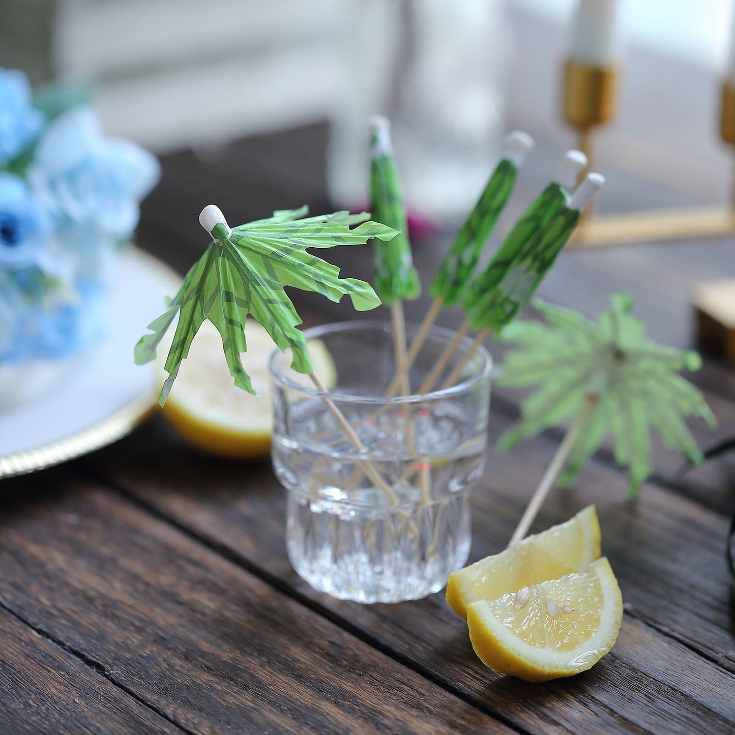 6" Green Tropical Leaf Cocktail Umbrella Picks in a glass with lemon slices.
