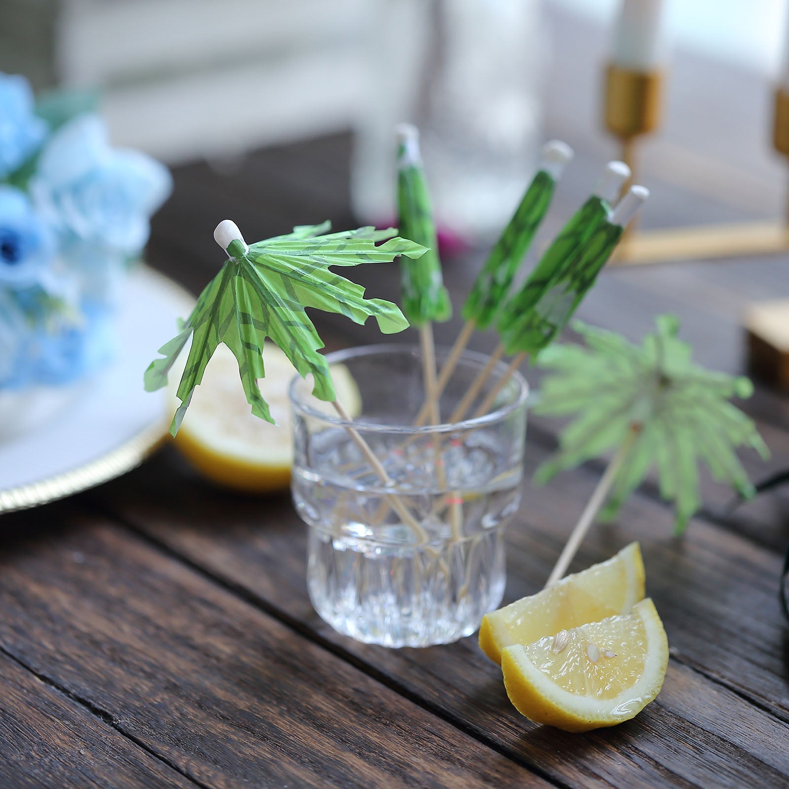 6" Green Tropical Leaf Cocktail Umbrella Picks in a glass with lemon slices.
