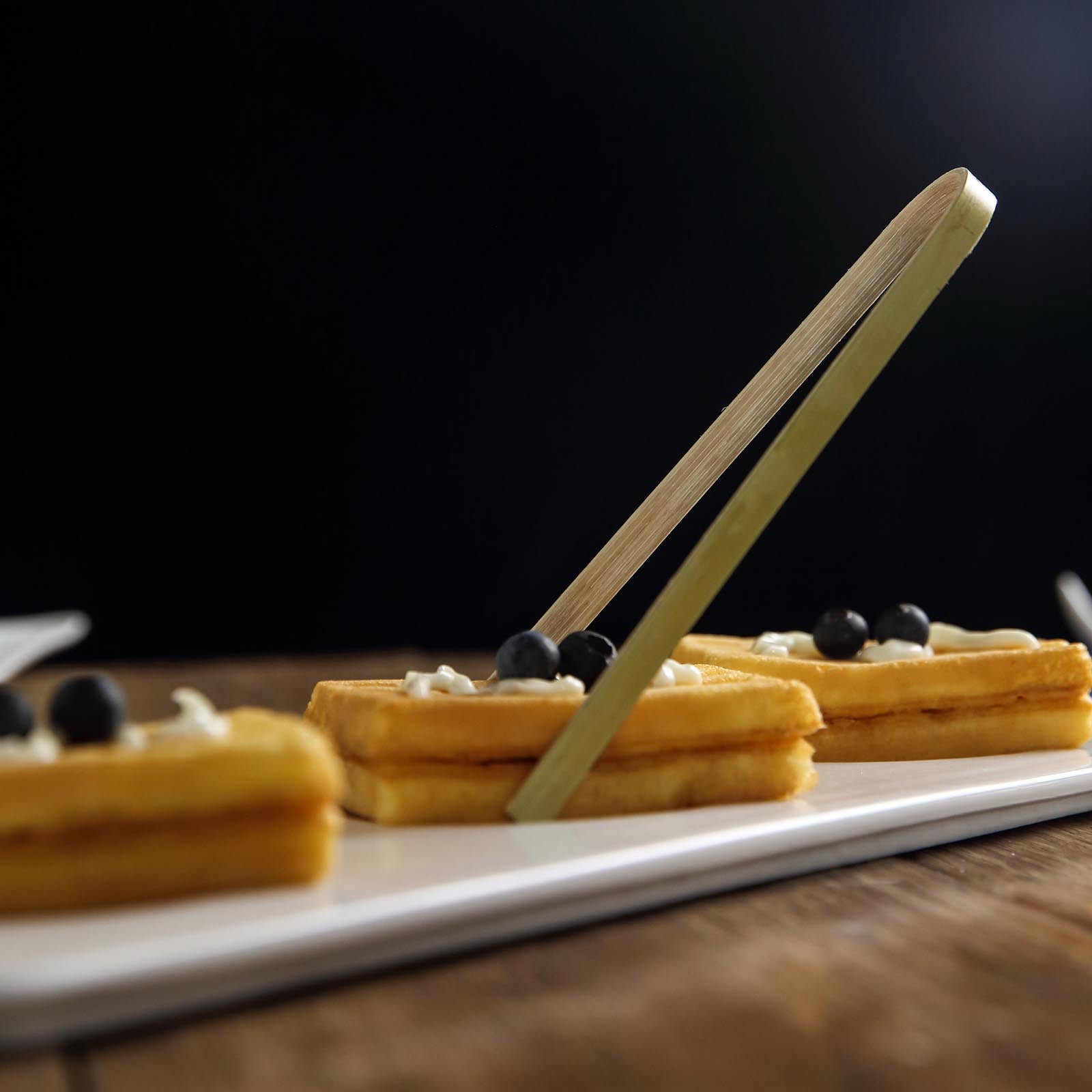 Eco-friendly natural bamboo tongs on a platter with waffles and blueberries.