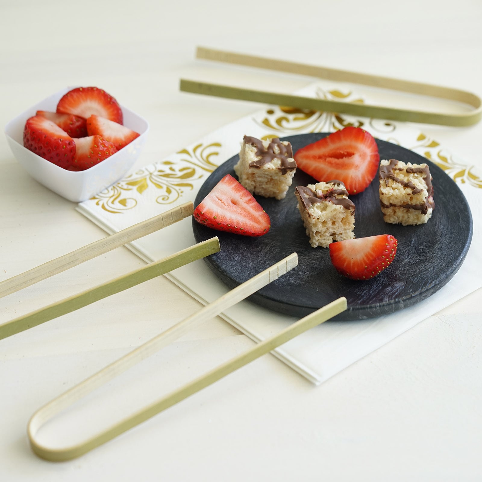 Eco-friendly bamboo tongs with strawberries on a plate.