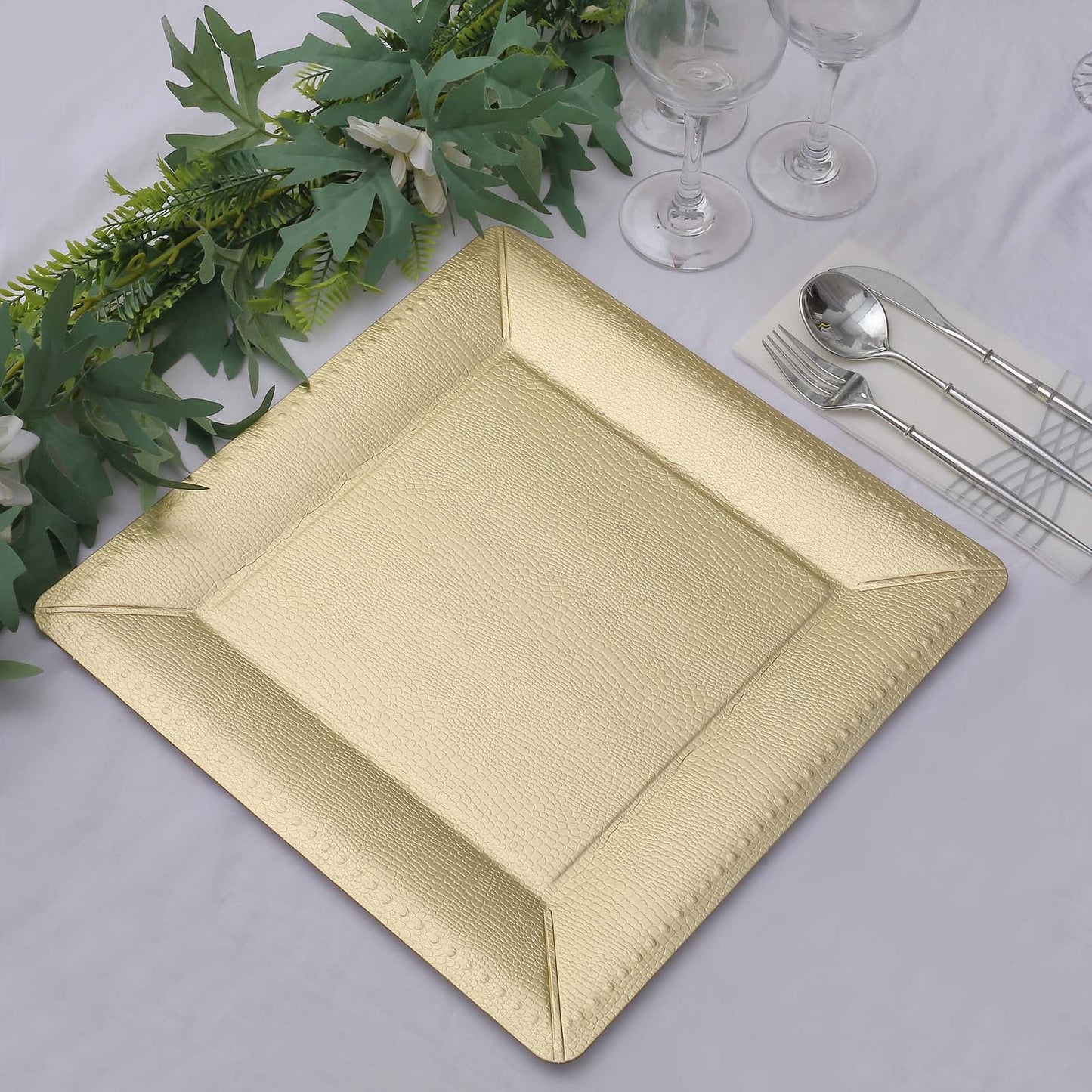 Champagne textured square serving tray on a table with greenery and glassware.