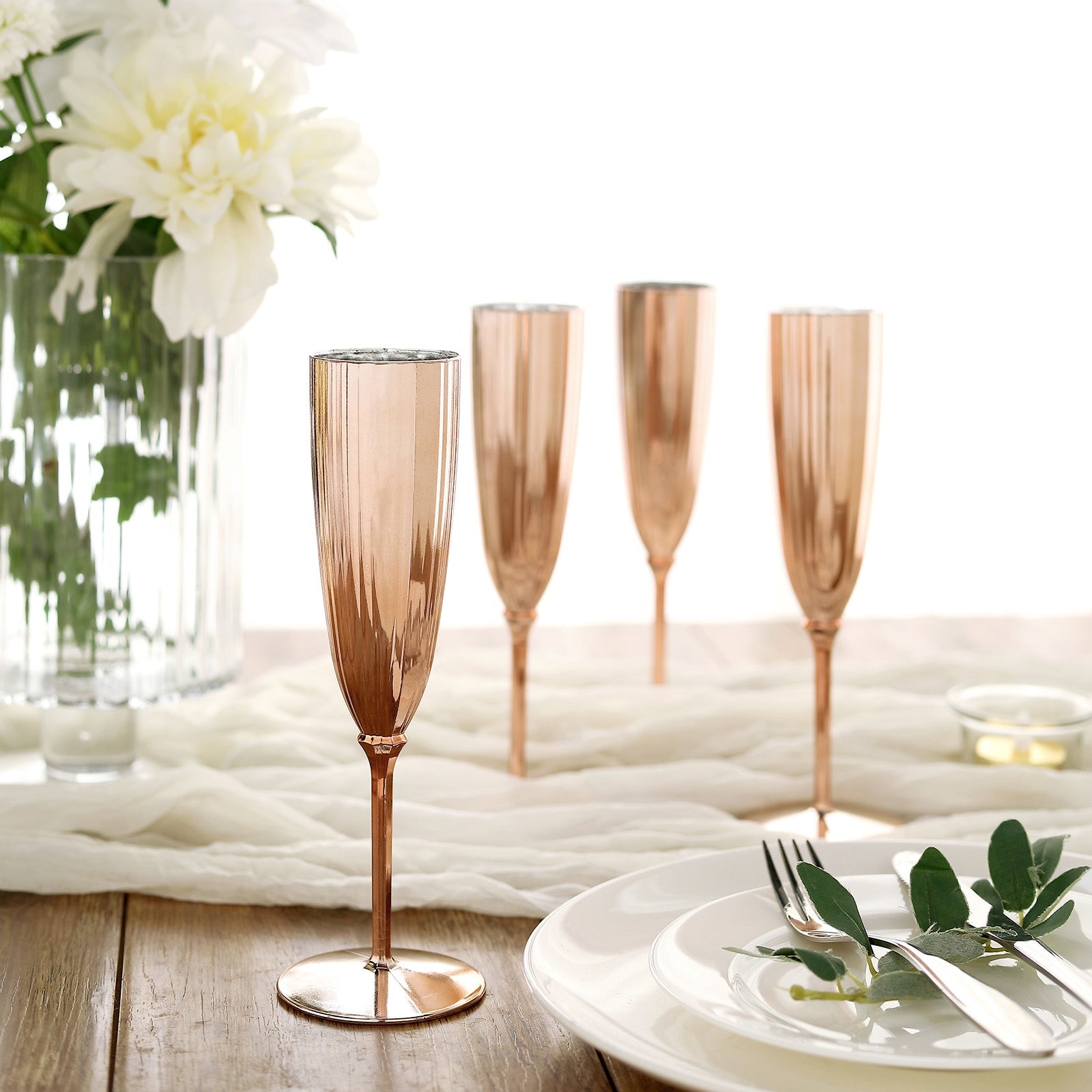Rose gold disposable champagne flutes set on a table with flowers.