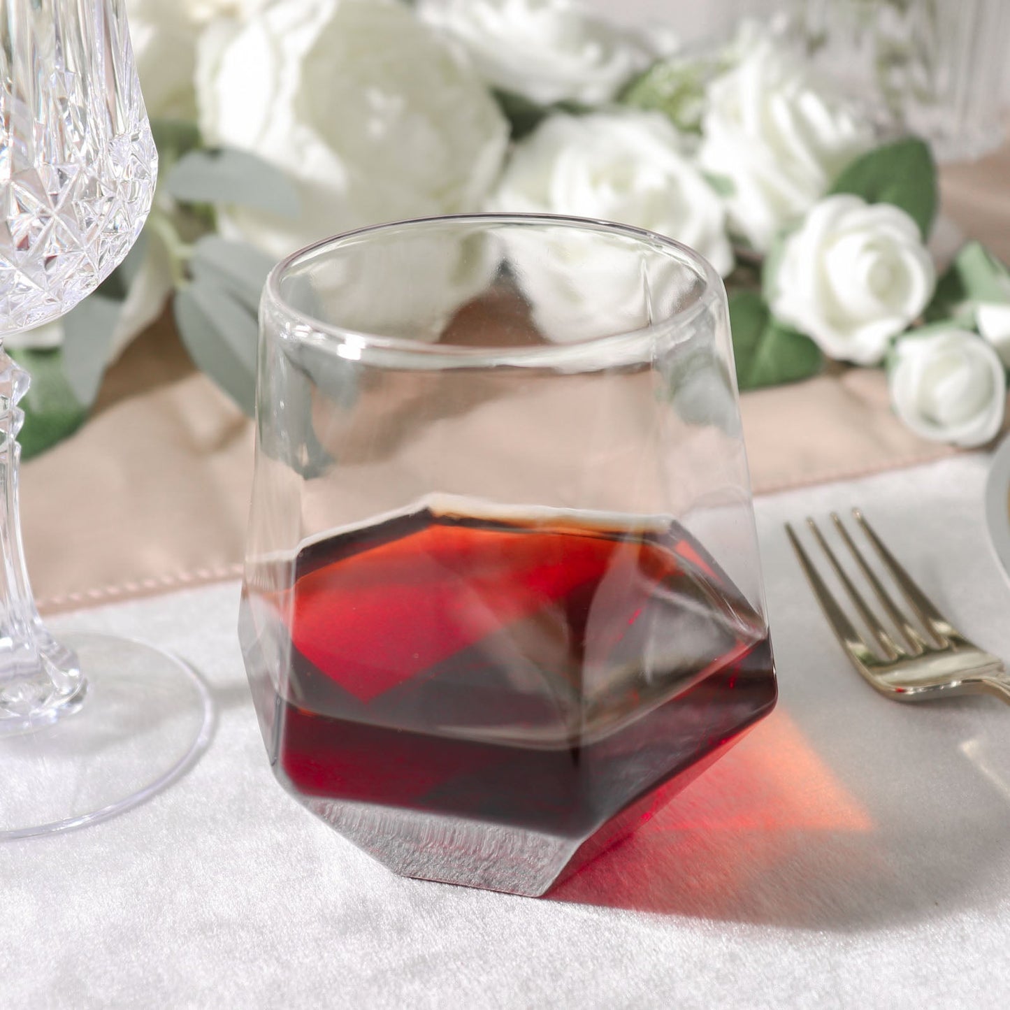 Clear diamond-shaped shatterproof whiskey cup with dark liquid inside.