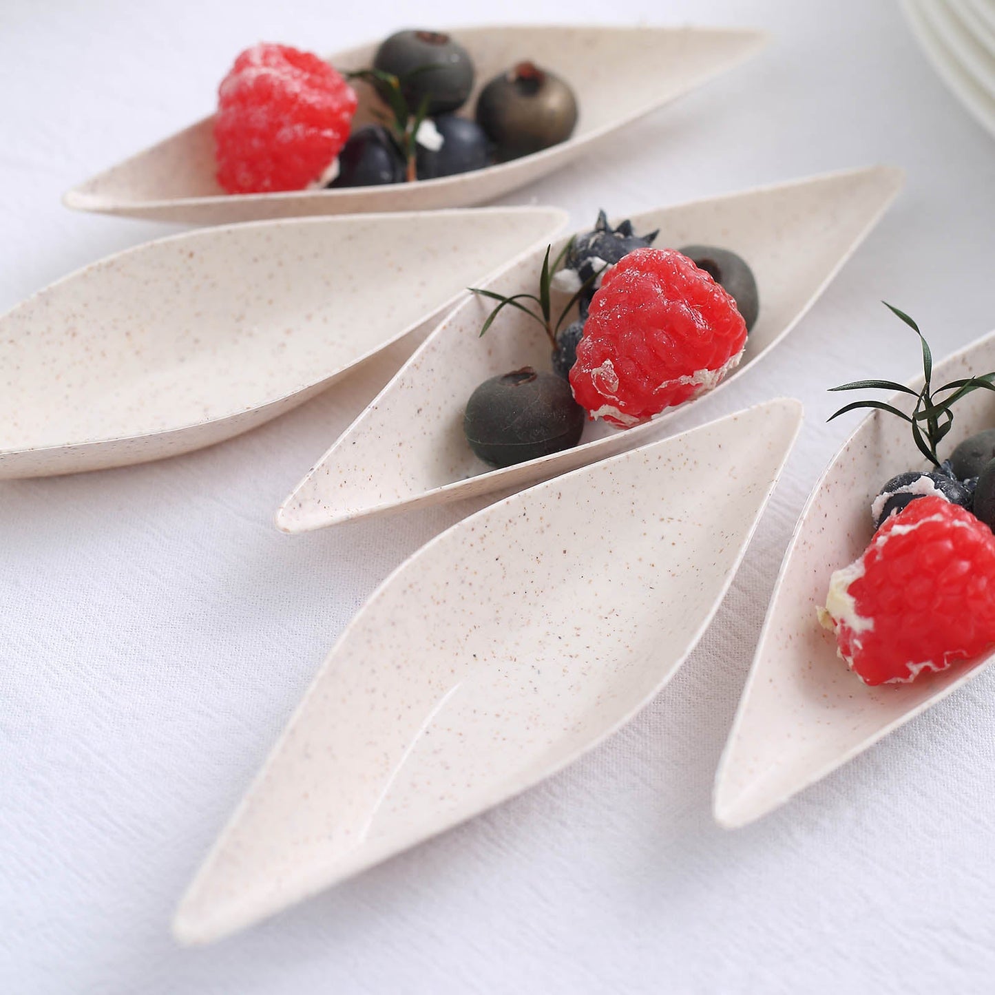 Biodegradable cream mini boat-shaped dessert plates with berries.