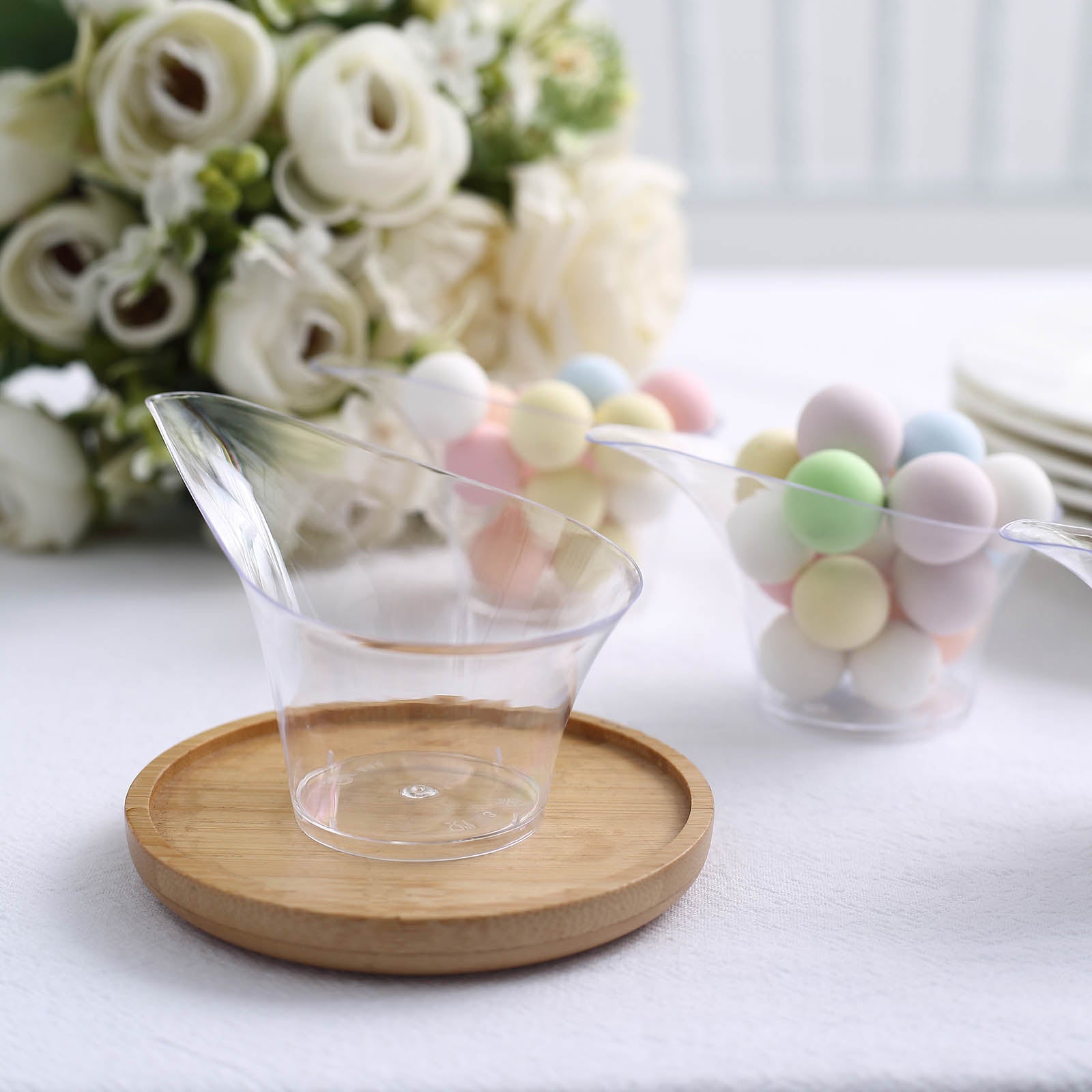 Clear mini disposable teardrop dessert cups on a wooden plate.