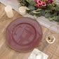 Elegant burgundy plate with gold trim, candles, and floral arrangement on a rustic table.