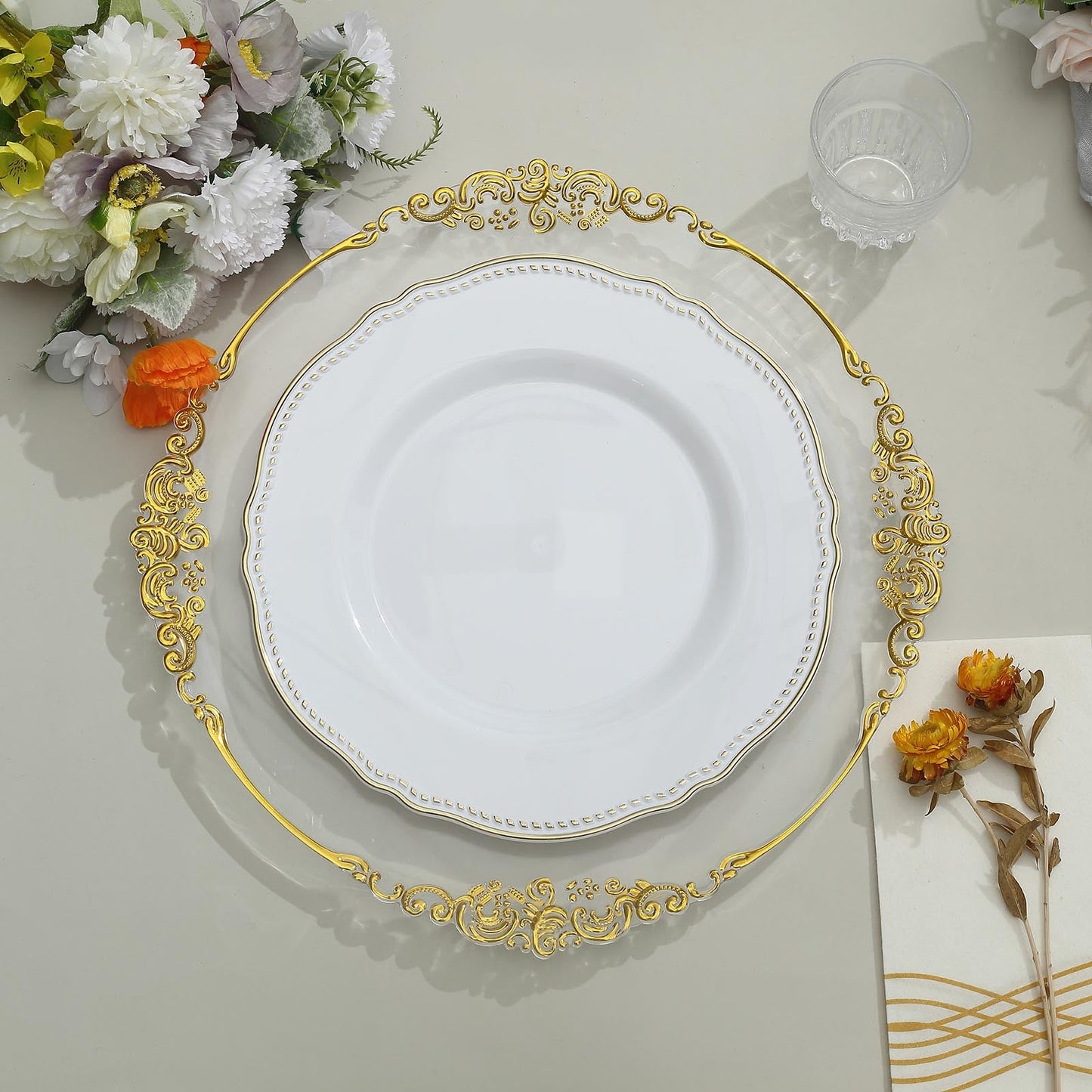 Elegant white plate with gold trim on decorative charger, surrounded by floral decor.