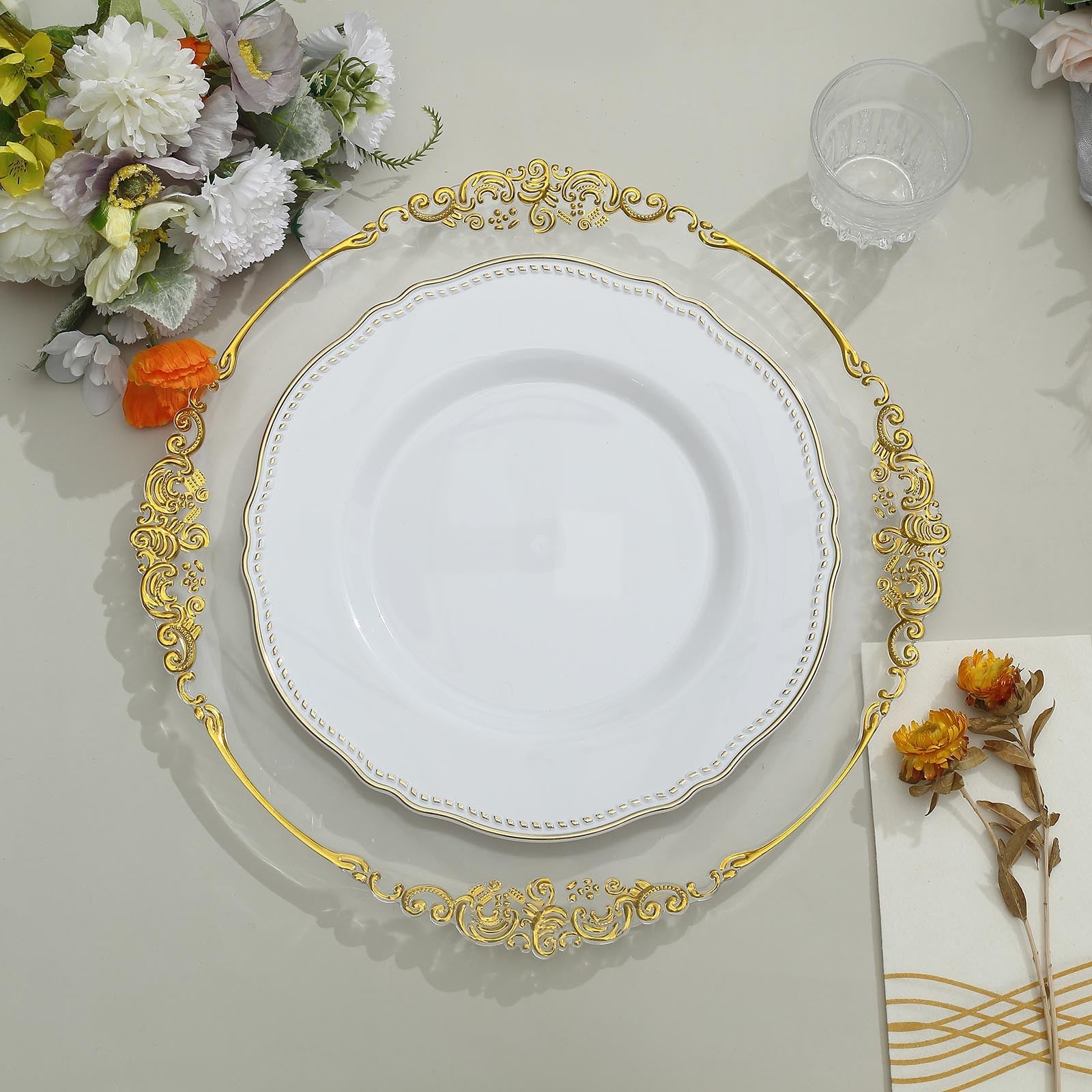 Elegant white plate with gold trim on decorative charger, surrounded by floral decor.