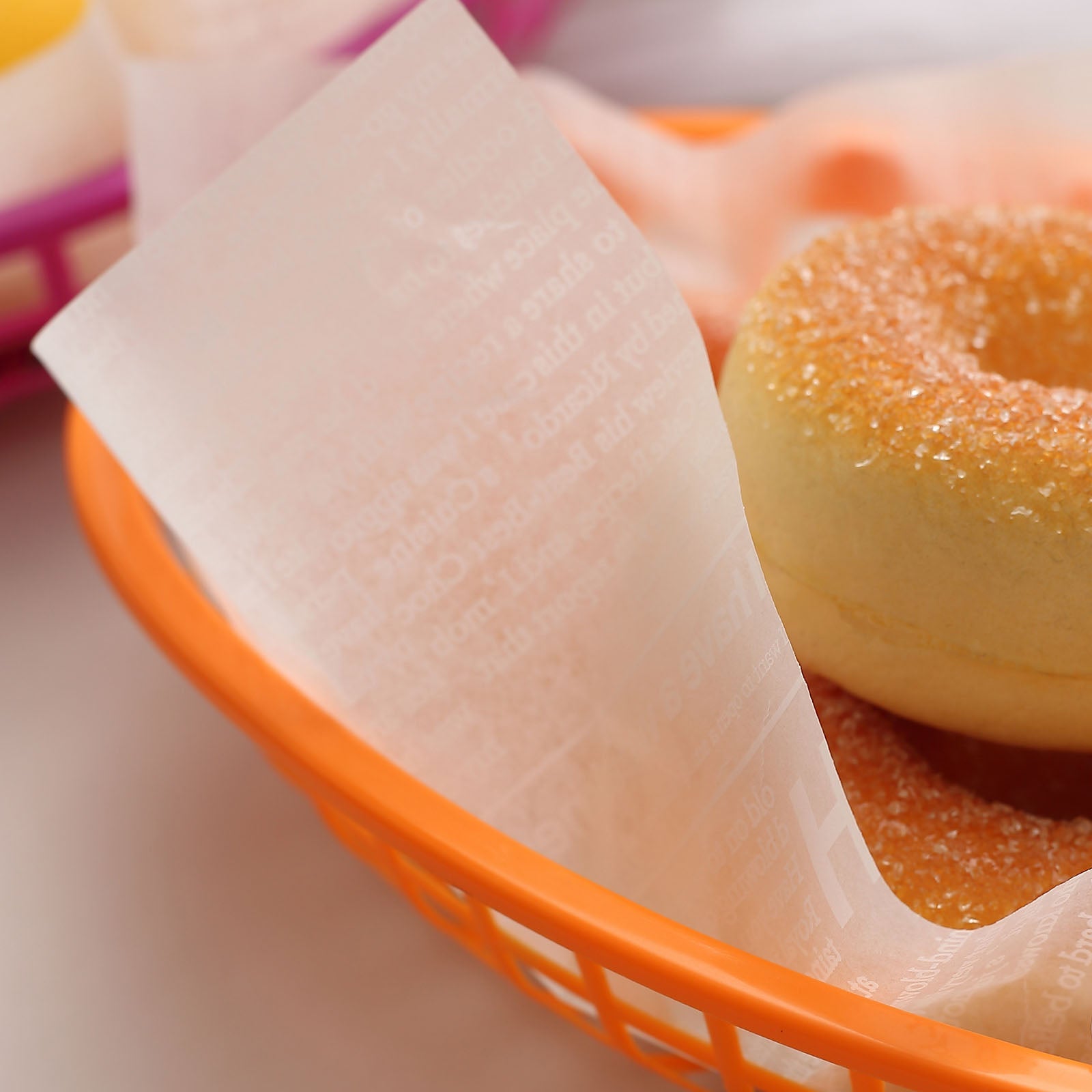 White wax paper food basket liner in an orange basket with donuts.