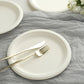 White biodegradable bagasse dinner plates with gold cutlery on a gray background.