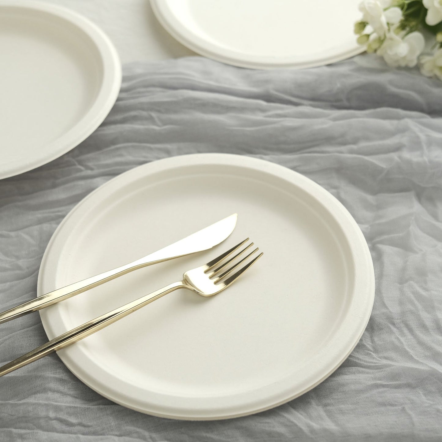 White biodegradable bagasse dinner plates with gold cutlery on a gray background.