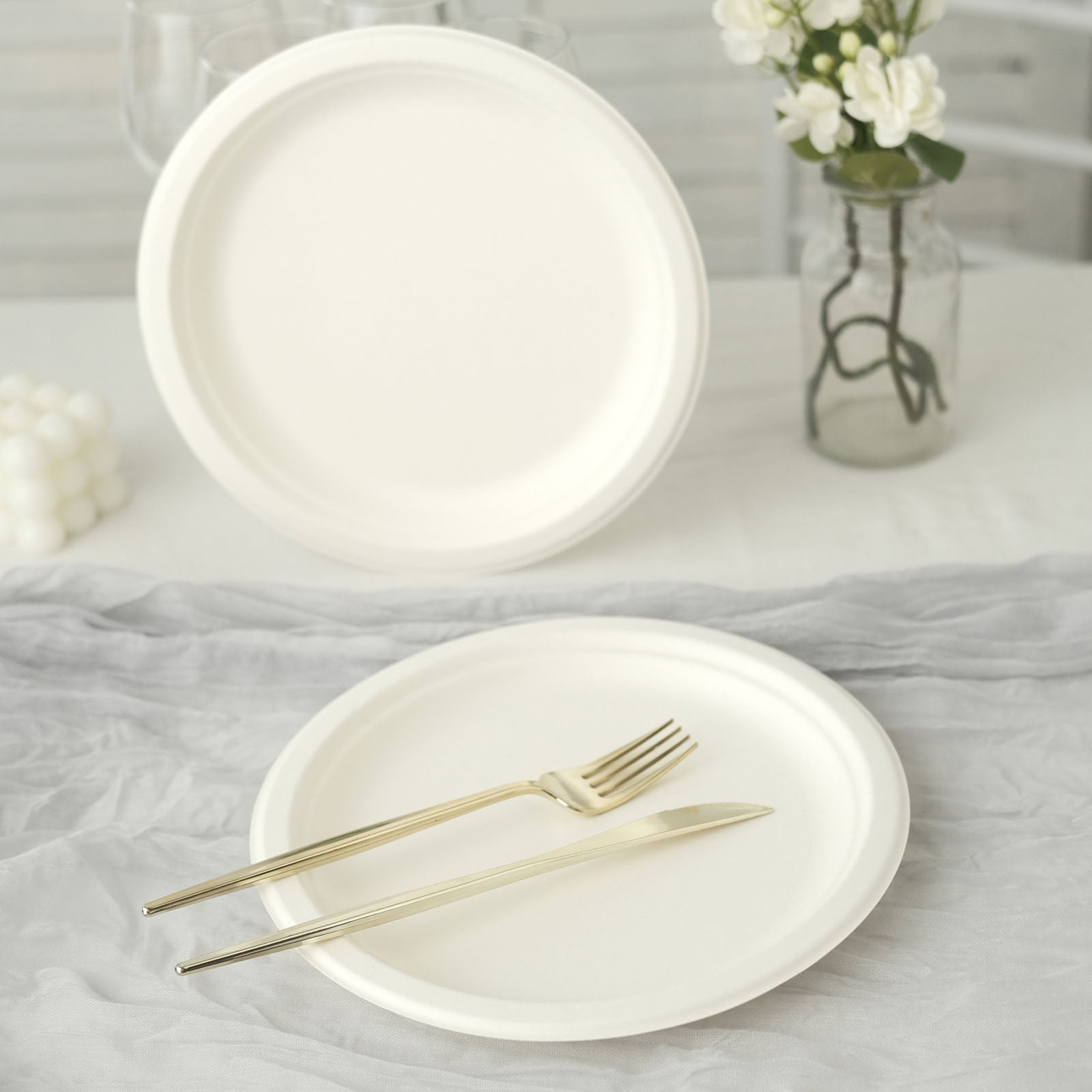 White biodegradable bagasse dinner plates on a table with gold utensils.