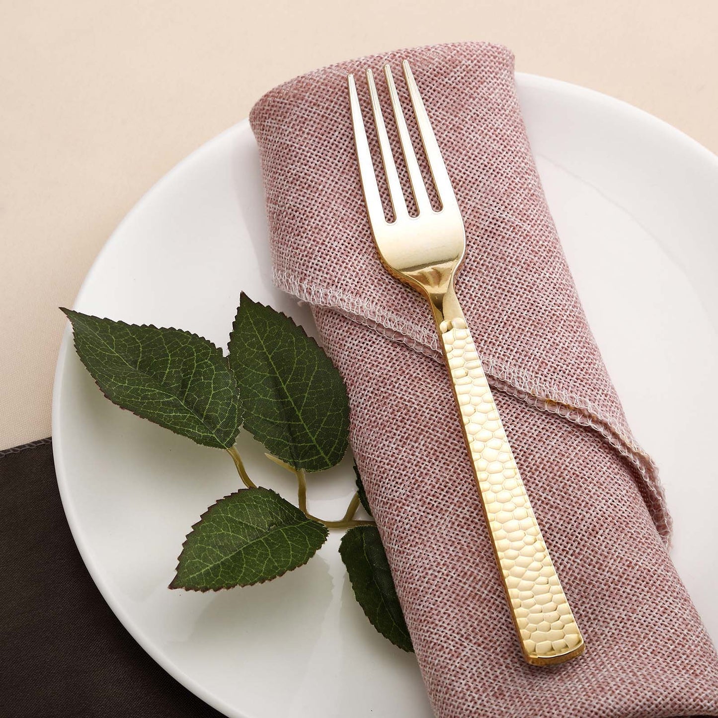 Gold hammered style heavy duty plastic fork on a plate with a napkin and leaves.