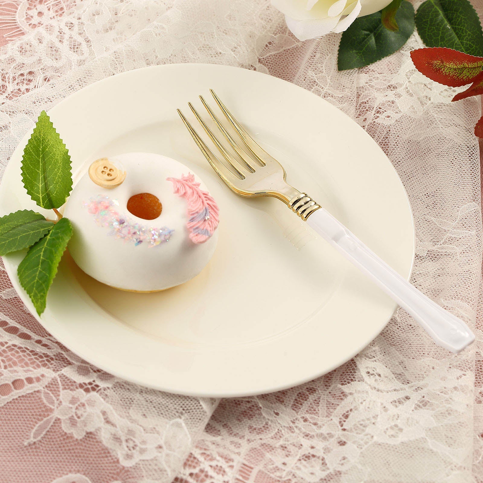 Gold plastic fork with white handle on a plate beside a decorated donut.